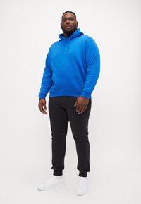 Sweatshirt azul com capuz e bolso frontal, combinado com calças de jogging pretas e ténis brancos. Design casual e confortável.
