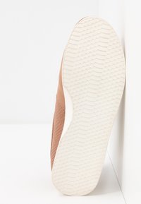 Baskets marron texturées avec une semelle en caoutchouc blanche, présentant un motif festonné sur la semelle et un design supérieur lisse.