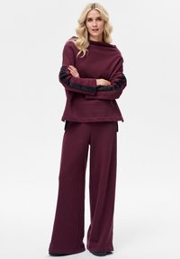 Bordeauxkleurige loungewear set met een loszittend shirt met zwarte, gestructureerde accenten op de mouwen en wijde broekspijpen, gemaakt van zachte stof.