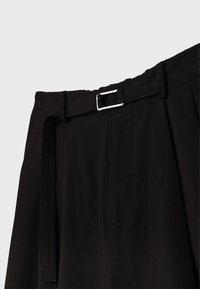 Pantaloni neri con una cintura ampia, caratterizzati da una parte anteriore piatta, passanti per cintura e una fibbia argentata. Tessuto liscio con pieghe strutturate.