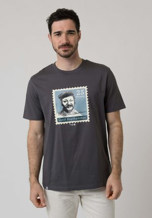 Man wearing dark gray T-shirt with a large stamp design featuring a bearded man, "25 Pfennig," and text "Gustl Bayrhammer."