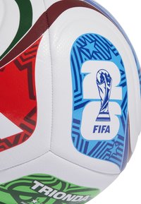 Zbliżenie na wielokolorową piłkę nożną Mistrzostw Świata FIFA 2018, na której widać logo trofeum oraz abstrakcyjne wzory w odcieniach czerwieni, zieleni i niebieskiego.