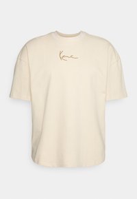 Cremfarbene Baumwoll-T-Shirt mit kurzen Ärmeln, rundem Ausschnitt und einem gestickten „Kane“-Logo in Gold auf der linken Brustseite.