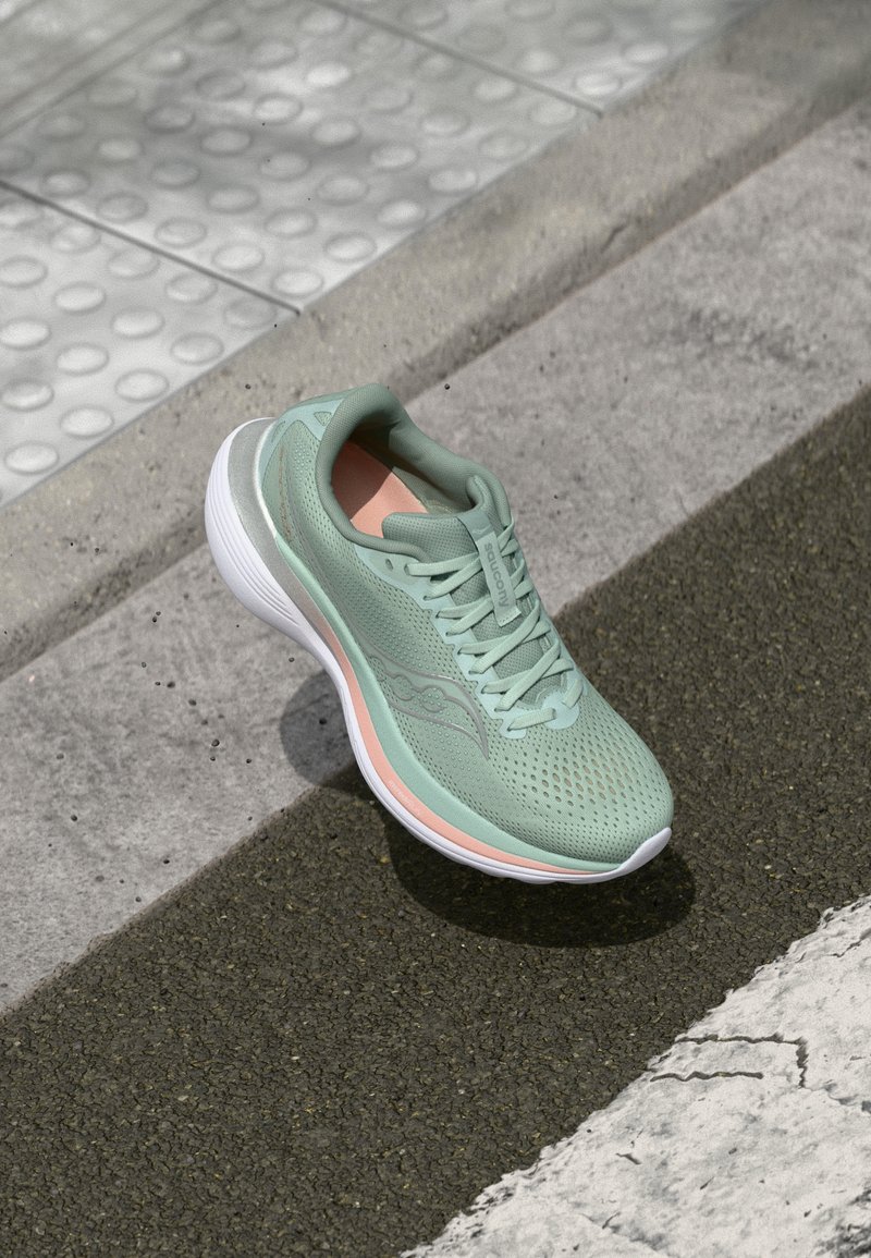Chaussure de sport vert clair avec une tige en mesh respirant, une semelle intermédiaire blanche et des accents pêche. Elle présente une pointe arrondie et une semelle texturée pour une meilleure adhérence.