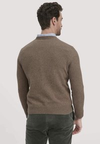 Brauner Strickpullover mit Rundhalsausschnitt und gerippten Bündchen, kombiniert mit strukturierten grünen Cordhosen. Schlichte Gestaltung, ohne sichtbare Muster.