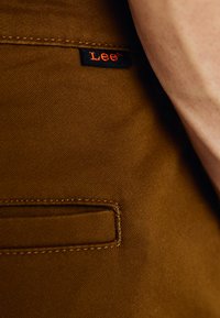 Brown fabric with a smooth texture, featuring a side pocket and a black label with red lettering that reads "Lee."