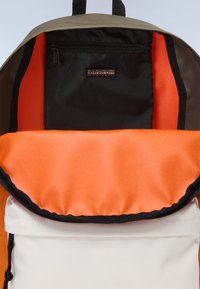 Ryggsäck med khakifärgad utsida, orange interiörfoder och en svart dragkedjeficka. Inkluderar en vit framficka med snörstängning.