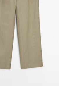 Pantalon beige à jambes larges avec des coutures visibles le long des côtés et de l’ourlet, présenté sur un fond blanc uni.