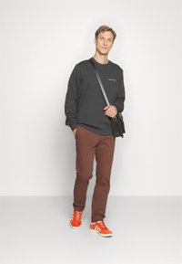 Felpa grigia scura, pantaloni marroni e sneakers arancioni con dettagli bianchi. Borsa a tracolla nera. Design semplice e linee pulite.