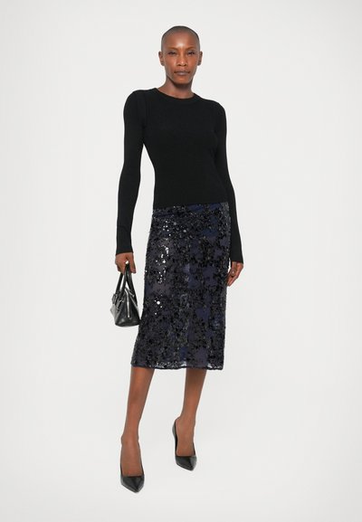 Top de malha preto de mangas longas combinado com uma saia lápis azul-marinho com lantejoulas. A modelo segura uma mala preta e usa saltos pretos com bico.