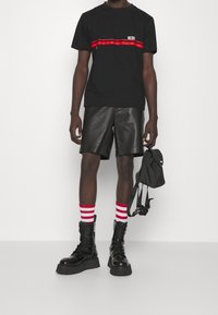 Camiseta negra con rayas rojas horizontales, combinada con pantalones cortos de cuero negros. Medias a rayas rojas y blancas, botas de combate negras y una mochila negra.