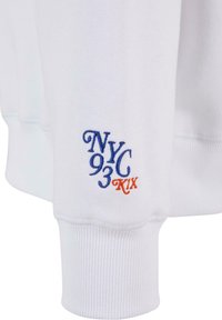 Witte sweatshirt met ribbels aan de mouwen, met "NYC 93 KIX" geborduurd in blauw en oranje op de onderarm voor contrast.