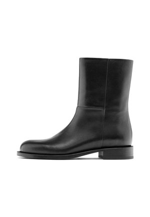 Bottine en cuir noir avec une texture lisse, un design minimaliste, un bout rond et un petit talon empilé. Pas de détails en métal visibles.