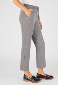 Schachbrett-Hose aus schwarz-weißer Stoff mit Kordelzugbund, seitlichen Taschen, geradem Bein und kombiniert mit schwarzen Slippern.