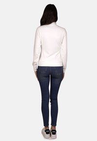 Maglietta bianca a maniche lunghe, dalla forma aderente, abbinata a jeans blu e sneakers nere. Tessuto liscio con dettagli a costine sui polsini e sull'orlo.