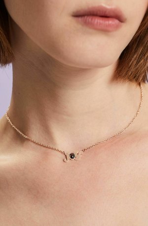 Rose gold necklace featuring a cursive "J" design with a small black gemstone at the center, set on a delicate chain.