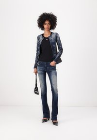 Chaqueta de mezclilla con un brillo azulado, camiseta negra, jeans acampanados de color azul desgastado y tacones negros de punta afilada; complementada con un pequeño bolso negro.