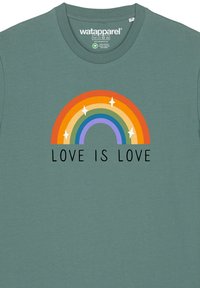 T-shirt en coton vert présentant un graphique arc-en-ciel multicolore avec des étoiles et le texte "L'AMOUR EST UN AMOUR" en noir en dessous.