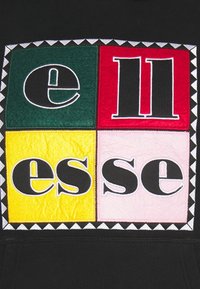 Černá mikina s kapucí, která má velkou čtvercovou barevnou nášivku s textem "ellesse" tučnými, blokovými písmeny. Barvy textu: zelená, červená, žlutá, růžová.