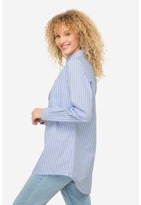Camisa de botones a rayas azul y blanca con mangas largas, bolsillos laterales, dobladillo curvado y un corte relajado, combinada con jeans de un azul claro.