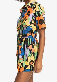 Blommönstrad kort rompers i livfulla färger—svart, gul, orange, grön och blå. Har krage, knappknäppning och belämd midja.