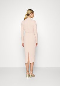 Vestido justo rosa com mangas longas, gola alta e abertura nas costas. Textura suave, comprimento até a metade da panturrilha e detalhes de alfaiataria discretos.
