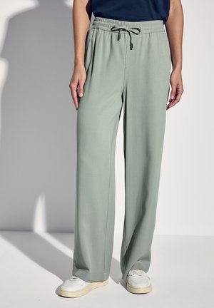 Light green wide-leg pants with an elastic waistband and drawstring. Smooth fabric with a relaxed fit, paired with white sneakers.