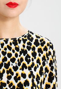 Top imprimé léopard en tissu léger et doux, avec des taches noires, jaunes et bleues ; encolure ronde ; et manches longues.