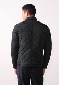 Black quilted jacket with a stand collar, featuring a diamond pattern, snap closures at the hem, and a smooth, shiny texture.