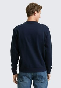 Granatowa bluza crewneck o fakturowanej powierzchni, z prążkowanymi mankietami i paskiem przy talii, noszona z jasnoniebieskimi dżinsami, widziana od tyłu.