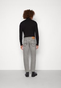 Musta pitkähihaine paita yhdistettynä harmaisiin suoriin farkkuihin, joissa on ruskea nahkapaikka ja sovitettu takataskut. Mustat nilkkurit viimeistelevät asun.