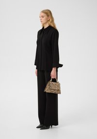 Camicia nera a strati e pantaloni a gamba larga abbinati a una piccola borsa a tracolla con stampa leopardata. Tessuto liscio con un design di borsa strutturato.