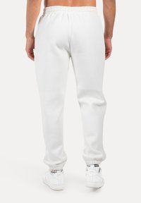 Weiße Jogginghosen mit elastischem Bund und Bündchen, die eine glatte Textur aufweisen. Getragen mit weißen Sneakern, die schwarze Akzente zeigen.