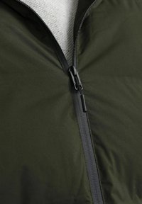 Chaqueta verde oliva con un acabado suave y mate; cuenta con un zipper negro y una textura interior gris. Cierre ubicado de forma central en la parte frontal.