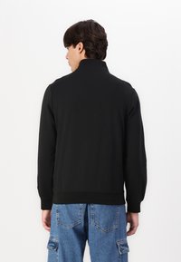 Must mustaga kõrge kaelusega, pikad varrukad ja soonikkoes mansetid, koos siniste cargo teksadega. Lihtne, ühtlane värvi disain.