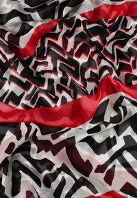Lekki szalik z odważnym, abstrakcyjnym wzorem w czerni, czerwieni i bieli. Materiał ma miękką, gładką fakturę i swobodnie się układa.