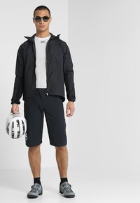 Black lightweight jacket, white mesh top, black shorts, gray cycling shoes. Holding a white helmet. Sunglasses added. Minimalist design.