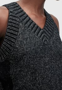 Svart ärmlös stickad topp med ett strukturerat mönster, med V-ringning och kontrasterande ribbade detaljer längs axlar och urringning.