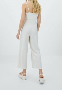 Une combinaison gris clair avec un motif texturé, un design à jambes larges et des bretelles ajustables. Portée avec des sandales à plateforme beiges.