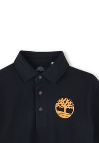 Polo shirt blu navy con una texture morbida, dotato di tre bottoni e di un logo ad albero arancione sulla parte sinistra del petto.