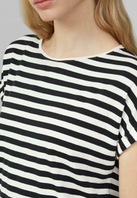 Frau trägt ein schwarz-weiß gestreiftes kurzärmliges Shirt mit rundem Halsausschnitt, gezeigt von den Schultern bis zum Kinn.