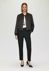 Zwarte bomberjack met ribgebreide manchetten, gecombineerd met slim-fit zwarte broeken. Witte blouse met een minimalistisch gezichtsdesign. Zwarte hoge hakken.