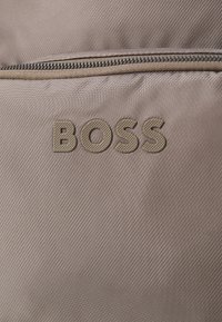 Pungă din țesătură maro cu o suprafață texturată, dotată cu închidere cu fermoar și logo-ul „BOSS” embosat într-o nuanță mai deschisă.