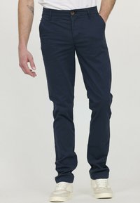 Chinos bleu marine en coton avec une coupe slim, dotés d'une fermeture à bouton à l'avant et de poches latérales, associés à des baskets blanches.