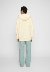 Cream-colored oversized hoodie with a drawstring hood, paired with light blue loose-fitting jeans. Soft texture, casual design.