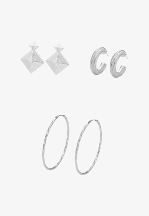 Drie paar zilveren oorbellen: linksboven geometrische vierkante studs, rechtsboven getextureerde kleine oorringen, onderaan grote dunne getextureerde oorringen op een witte achtergrond.