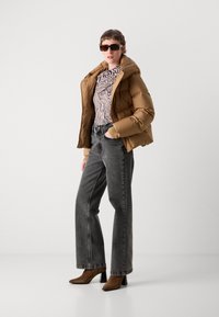 Veste matelassée marron, haut rayé noir et blanc, jean gris taille haute, bottines à talons marron, et lunettes de soleil sombres avec une monture carrée.