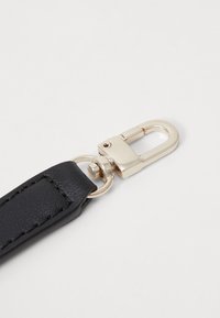 Mousqueton pivotant en métal attaché à une lanière en cuir noir cousue, sur un fond blanc uni.