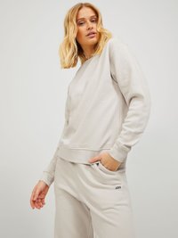 Felpa grigia chiara con polsini e orlo a coste, realizzata in materiale morbido. Abbinata a pantaloni coordinati con un piccolo logo nero.