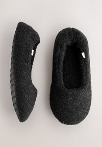 Pantofole in feltro nero con una texture morbida, forma rotonda e suole in gomma con motivo. Nessun marchio visibile sulla parte superiore.